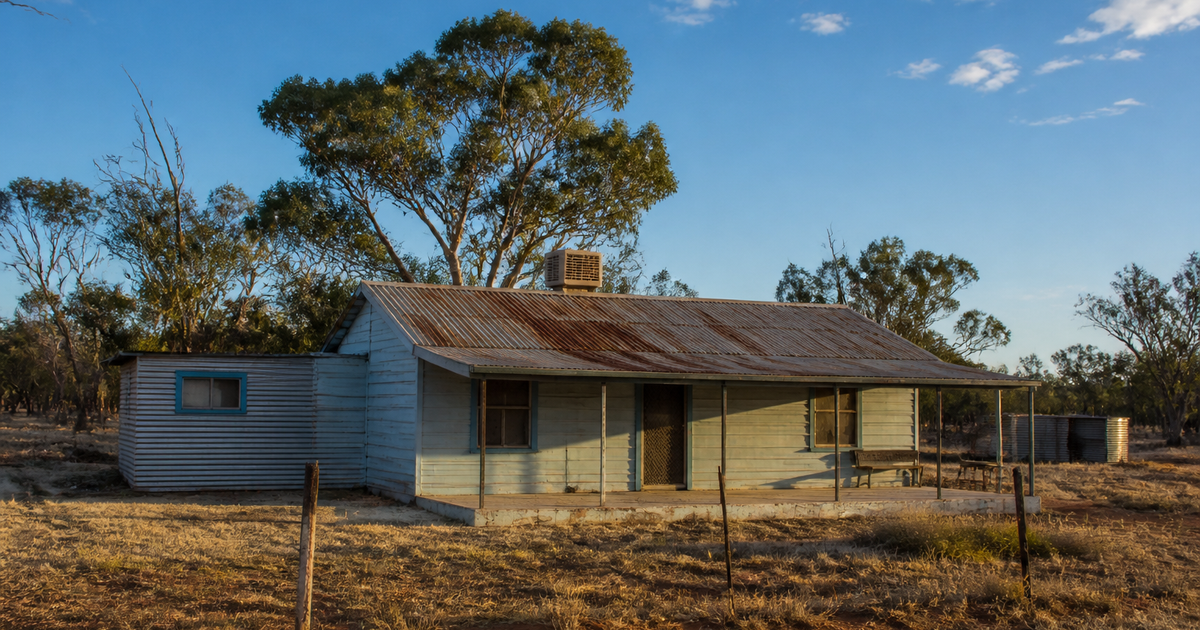 Weathered single-storey house with a rusting corrugated iron roof and open verandah in a remote northern Australian community at late afternoon