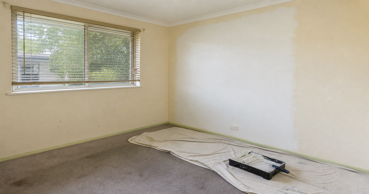 Rental bedroom mid-repaint with roller tray and drop sheets