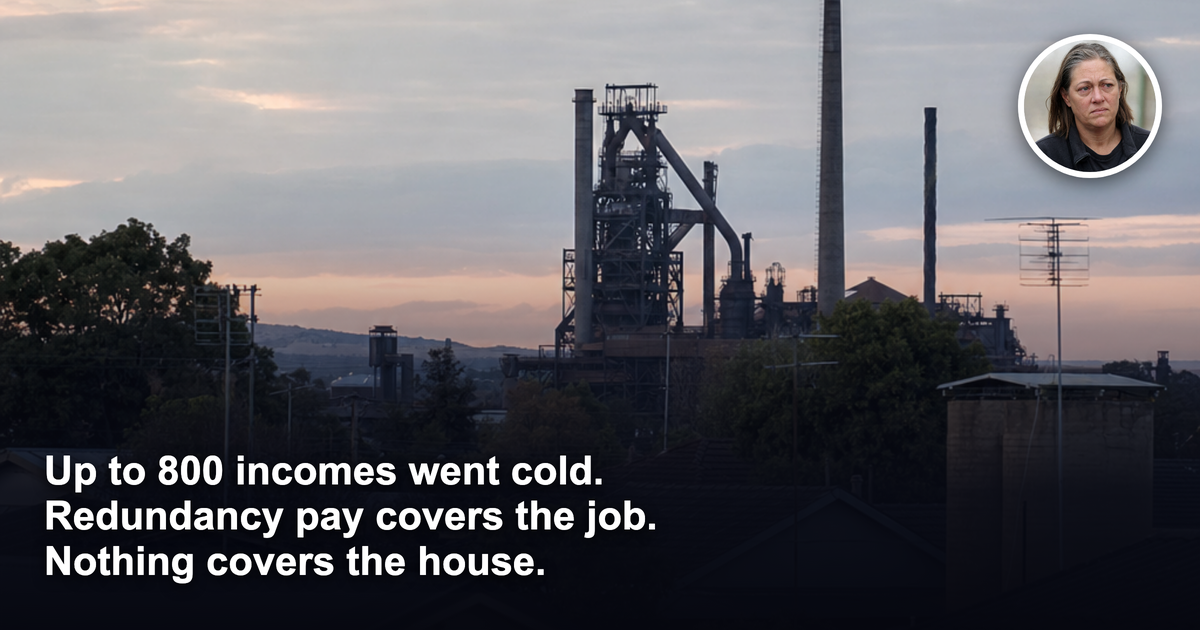 A cold, silent steelworks blast furnace on the horizon behind the rooftops of modest single-storey brick-and-tile houses at dusk